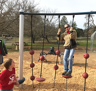 Staff member using a playground jungle gym with a student outside